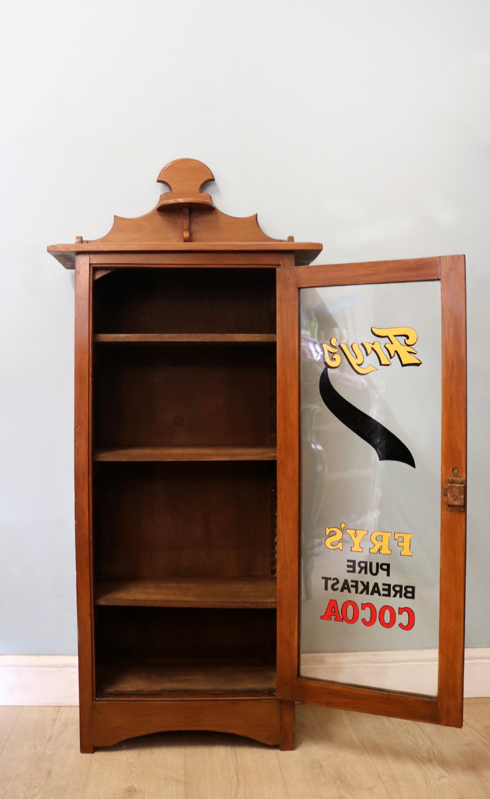 A Victorian American walnut glazed display cabinet featuring a shaped top pediment and hand-painted Frys Chocolate advertising on the single glass door. View III