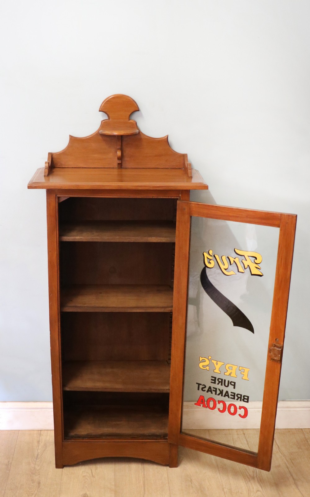 A Victorian American walnut glazed display cabinet featuring a shaped top pediment and hand-painted Frys Chocolate advertising on the single glass door. View IV