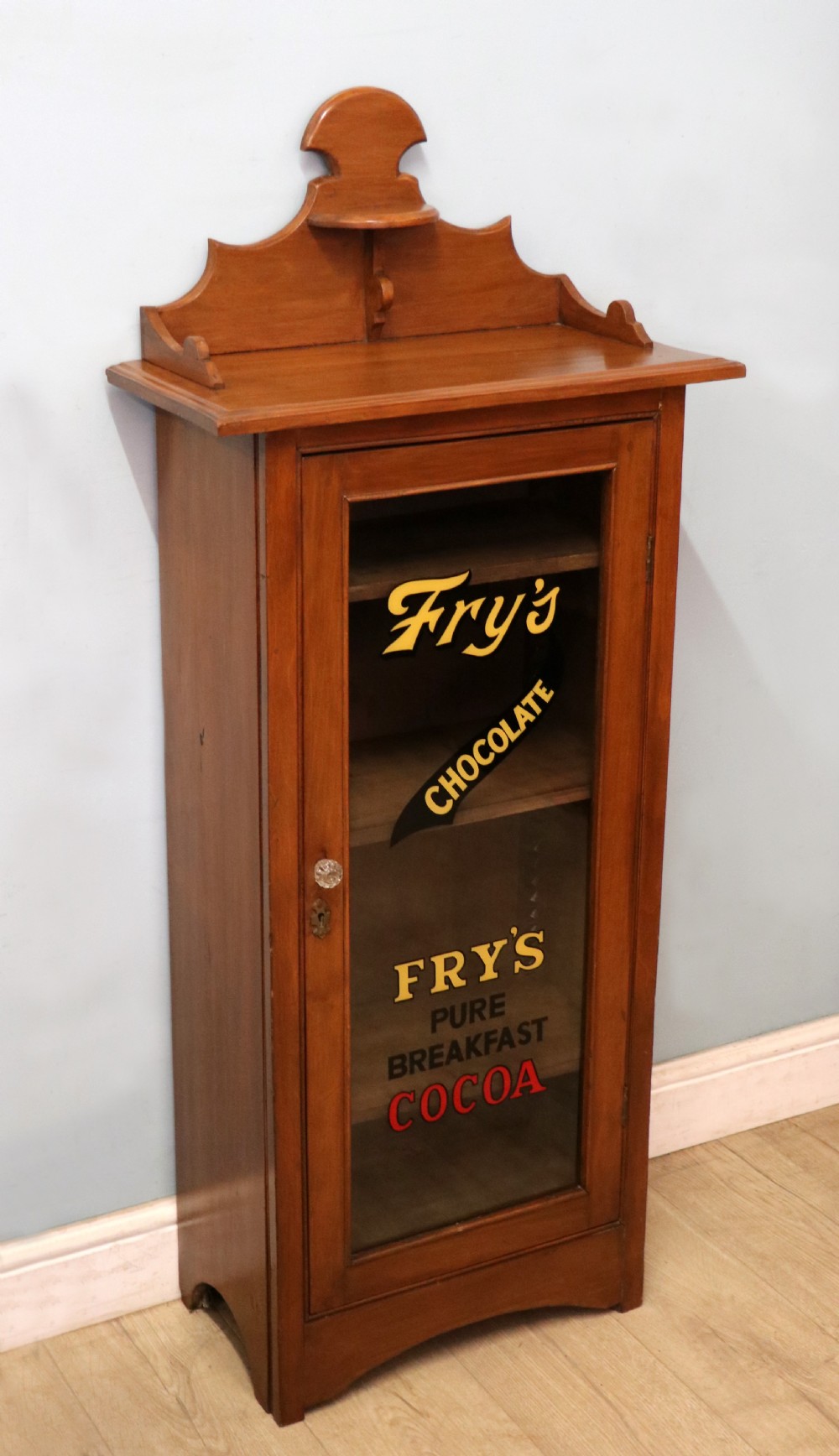 A Victorian American walnut glazed display cabinet featuring a shaped top pediment and hand-painted Frys Chocolate advertising on the single glass door. View V