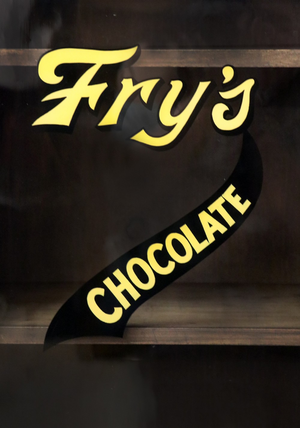 A Victorian American walnut glazed display cabinet featuring a shaped top pediment and hand-painted Frys Chocolate advertising on the single glass door. View XIII