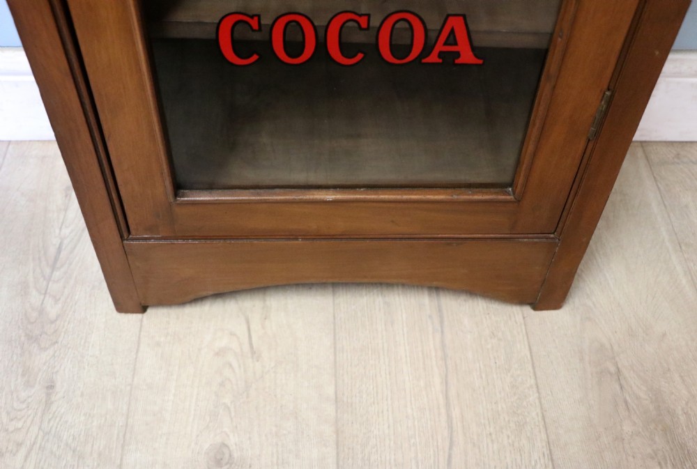 A Victorian American walnut glazed display cabinet featuring a shaped top pediment and hand-painted Frys Chocolate advertising on the single glass door. View XXIV