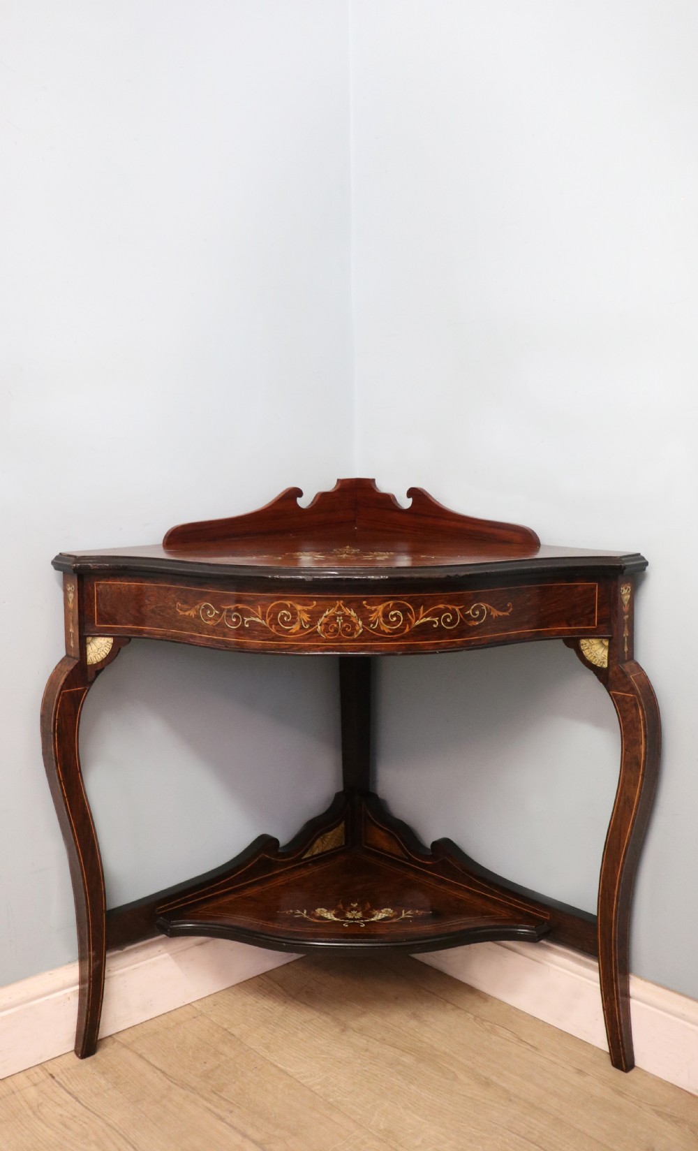 An early twentieth-century Sheraton Revival mahogany corner table featuring elaborate floral marquetry inlay, curved legs, and an undertier shelf.