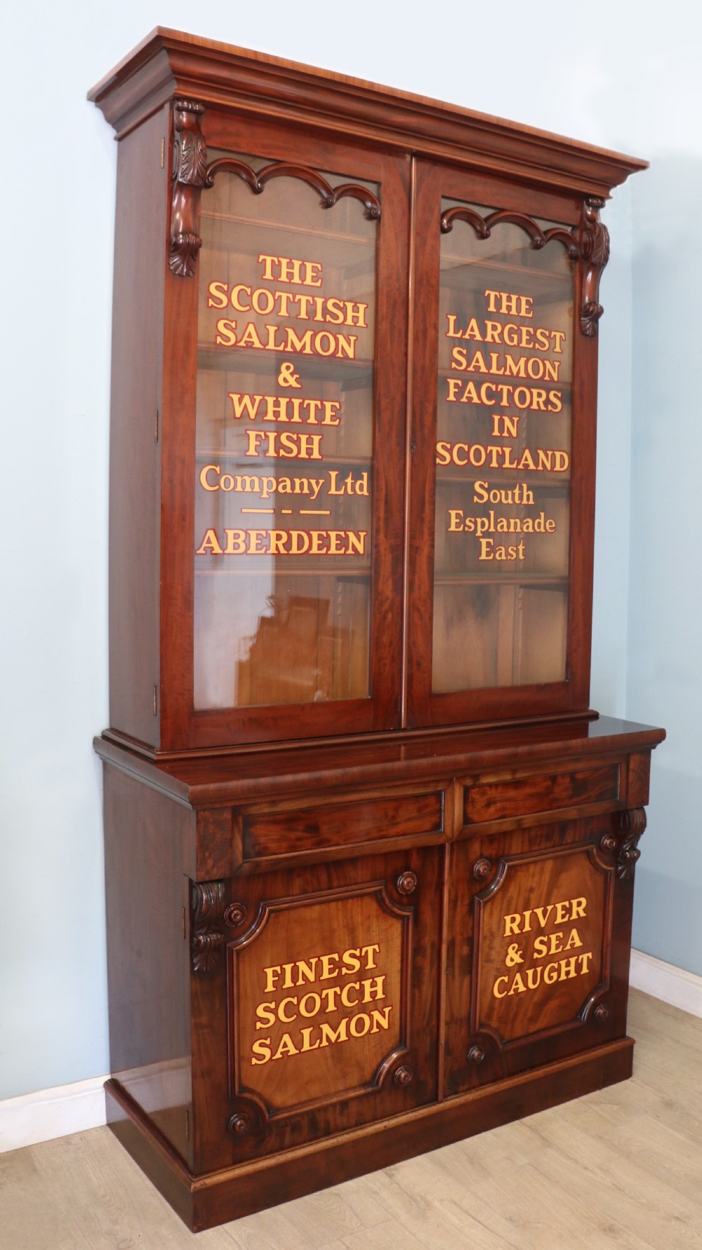 A Victorian mahogany two-height glazed bookcase featuring gilt advertising lettering on the glass doors and lower panelled doors.