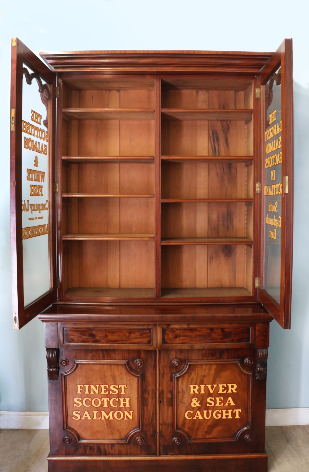A Victorian mahogany two-height glazed bookcase featuring gilt advertising lettering on the glass doors and lower panelled doors. View II