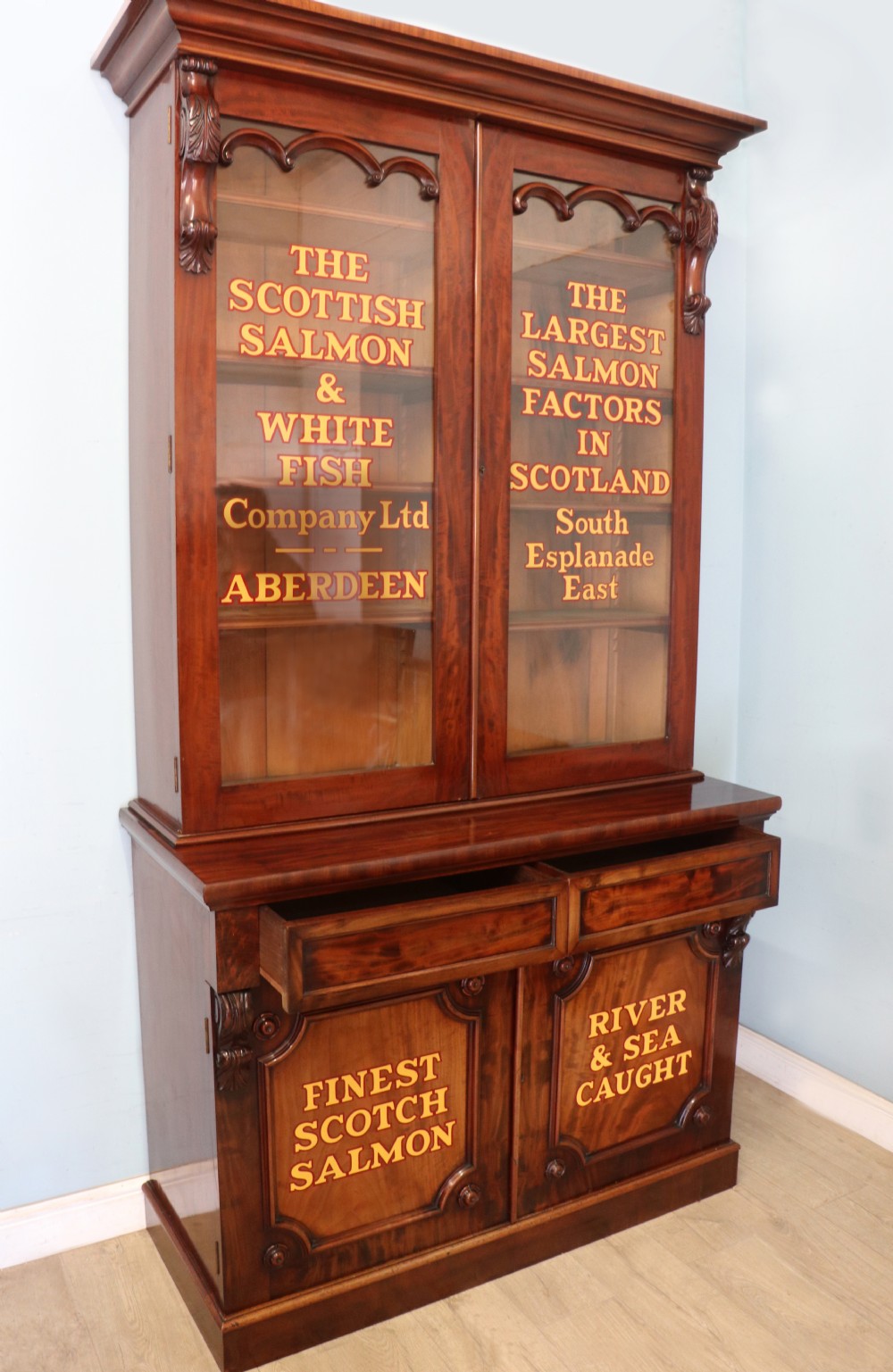 A Victorian mahogany two-height glazed bookcase featuring gilt advertising lettering on the glass doors and lower panelled doors. View III