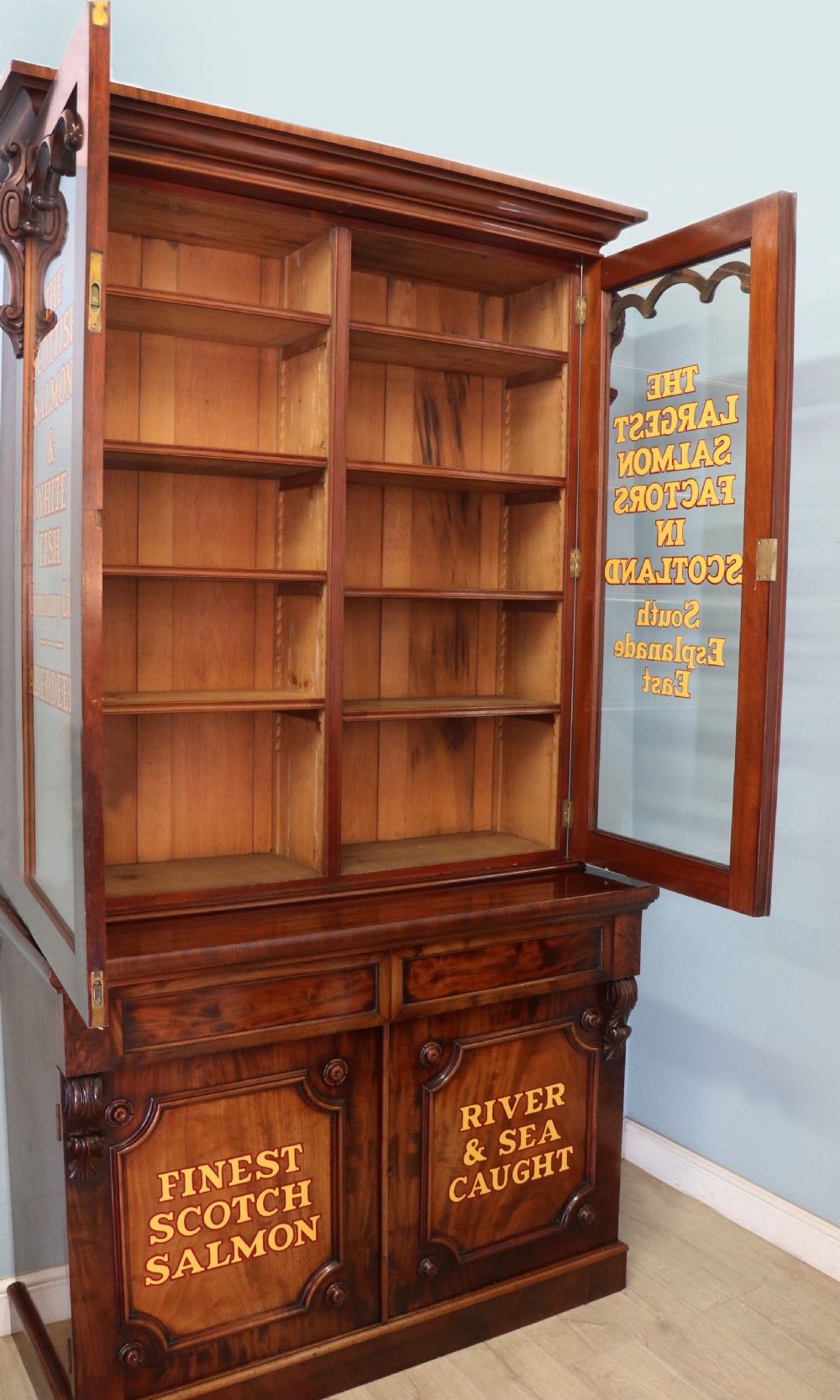 A Victorian mahogany two-height glazed bookcase featuring gilt advertising lettering on the glass doors and lower panelled doors. View V