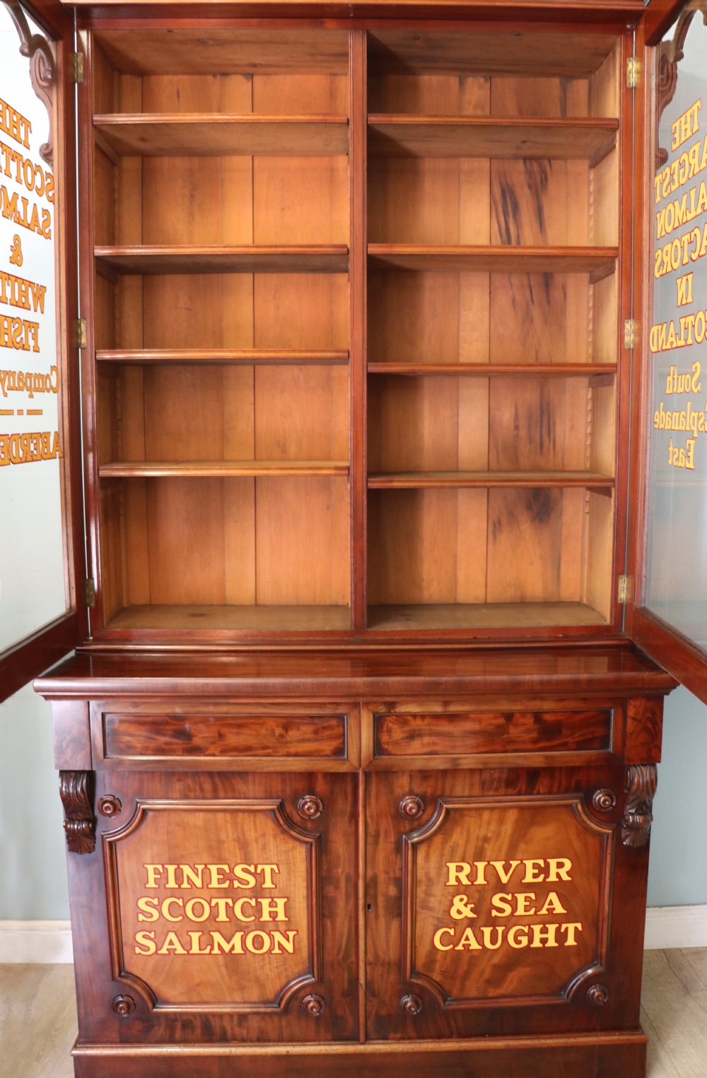 A Victorian mahogany two-height glazed bookcase featuring gilt advertising lettering on the glass doors and lower panelled doors. View VI