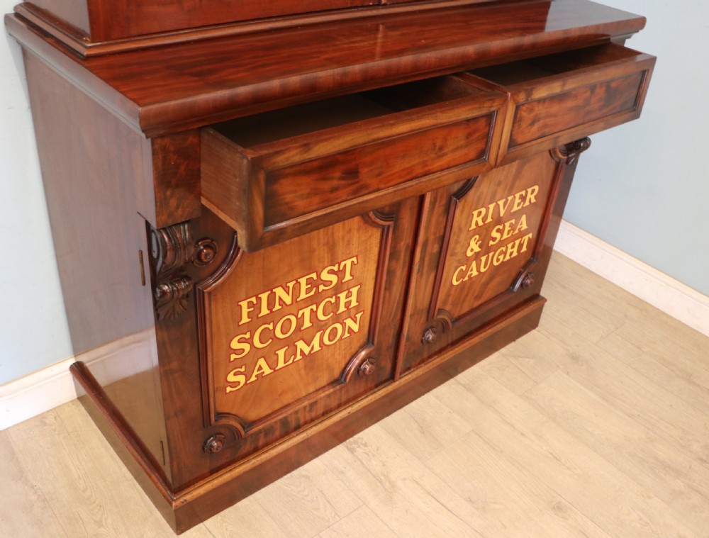 A Victorian mahogany two-height glazed bookcase featuring gilt advertising lettering on the glass doors and lower panelled doors. View XXIX