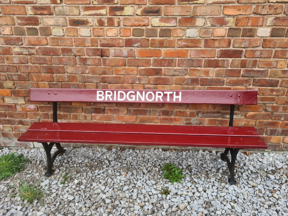 A late nineteenth to early twentieth-century painted maroon wooden railway bench featuring black cast-iron supports and white text reading BRIDGNORTH across the backrest.