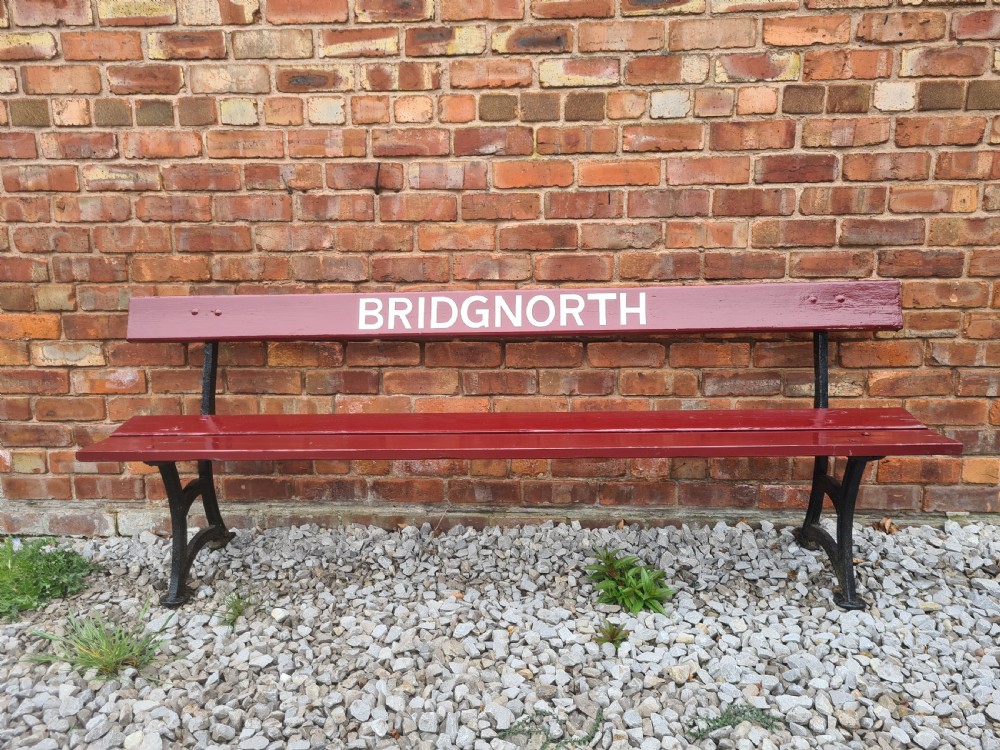 A late nineteenth to early twentieth-century painted maroon wooden railway bench featuring black cast-iron supports and white text reading BRIDGNORTH across the backrest. View II
