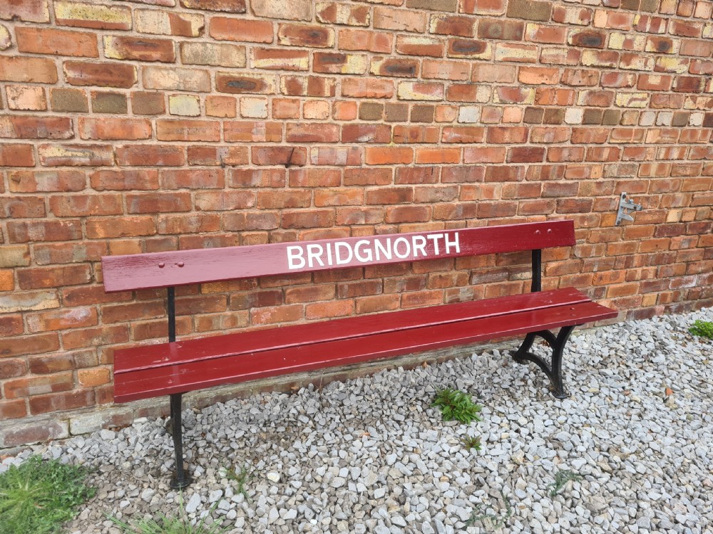 A late nineteenth to early twentieth-century painted maroon wooden railway bench featuring black cast-iron supports and white text reading BRIDGNORTH across the backrest. View III