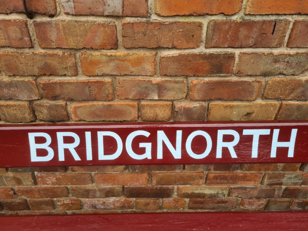 A late nineteenth to early twentieth-century painted maroon wooden railway bench featuring black cast-iron supports and white text reading BRIDGNORTH across the backrest. View IV