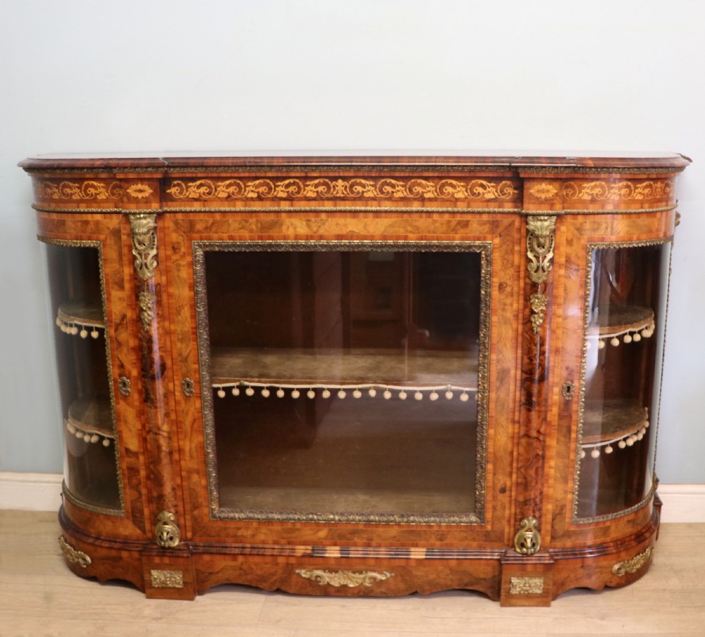 A Victorian walnut credenza featuring floral marquetry inlay, a central glazed door, two curved glass side doors, and gilt metal mounts.