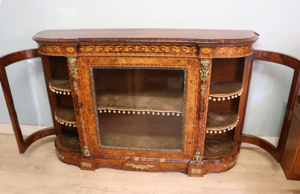 A Victorian walnut credenza featuring floral marquetry inlay, a central glazed door, two curved glass side doors, and gilt metal mounts. View V