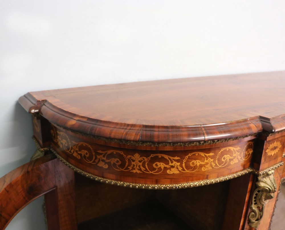 A Victorian walnut credenza featuring floral marquetry inlay, a central glazed door, two curved glass side doors, and gilt metal mounts. View X