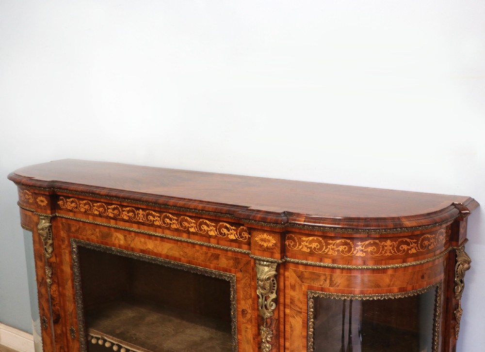 A Victorian walnut credenza featuring floral marquetry inlay, a central glazed door, two curved glass side doors, and gilt metal mounts. View XIV