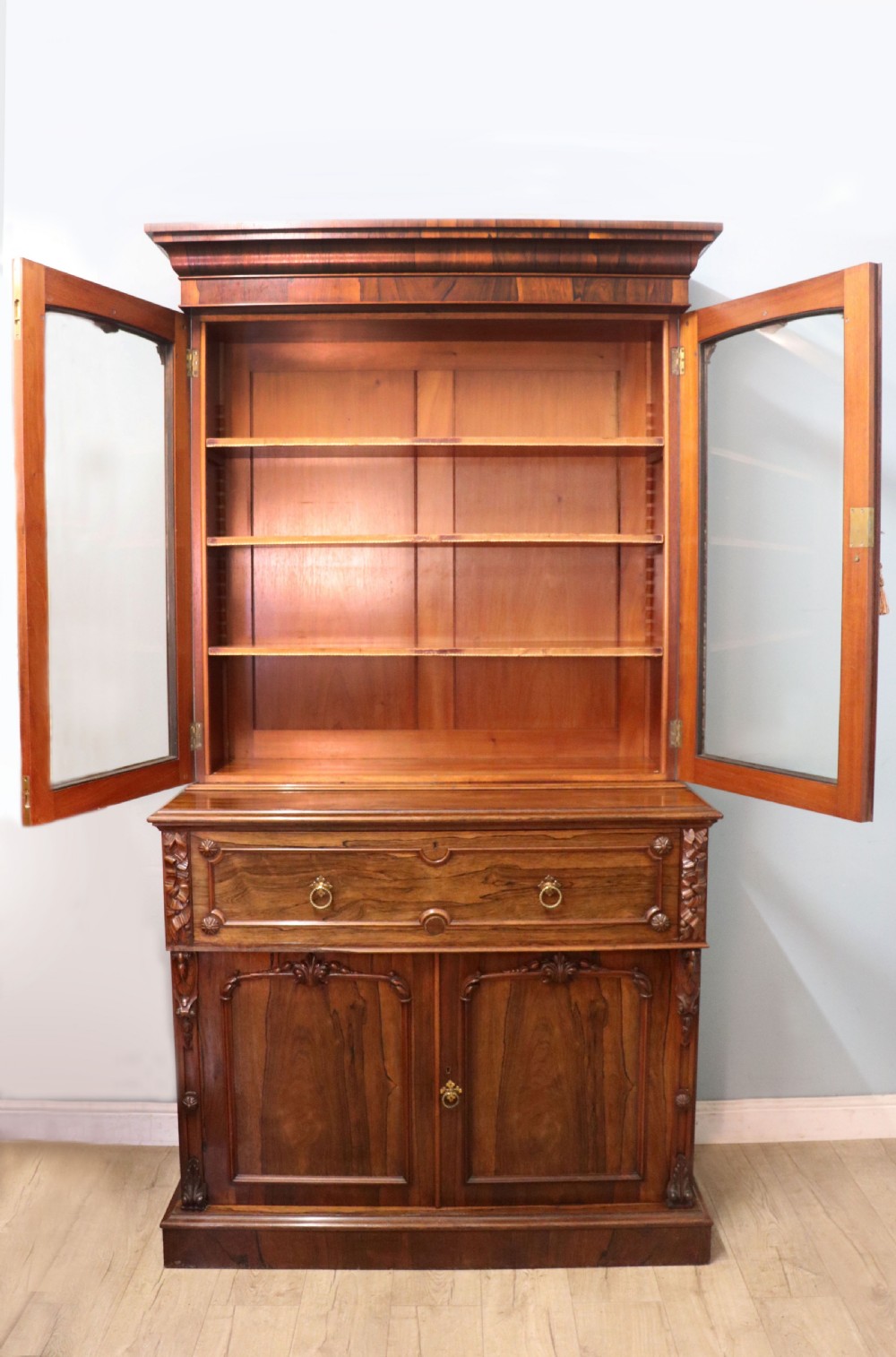 An early Victorian glazed secretaire bookcase cabinet in dark figured wood with carved arch details, a central desk drawer, and lower cupboard doors. View II