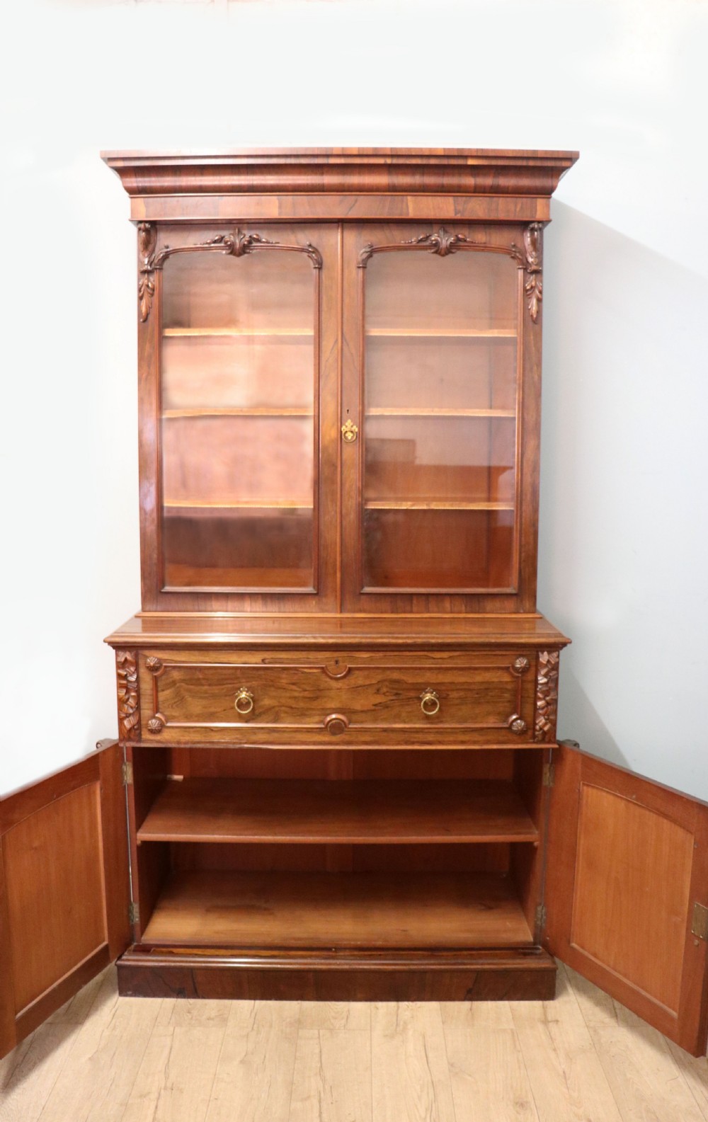 An early Victorian glazed secretaire bookcase cabinet in dark figured wood with carved arch details, a central desk drawer, and lower cupboard doors. View IV