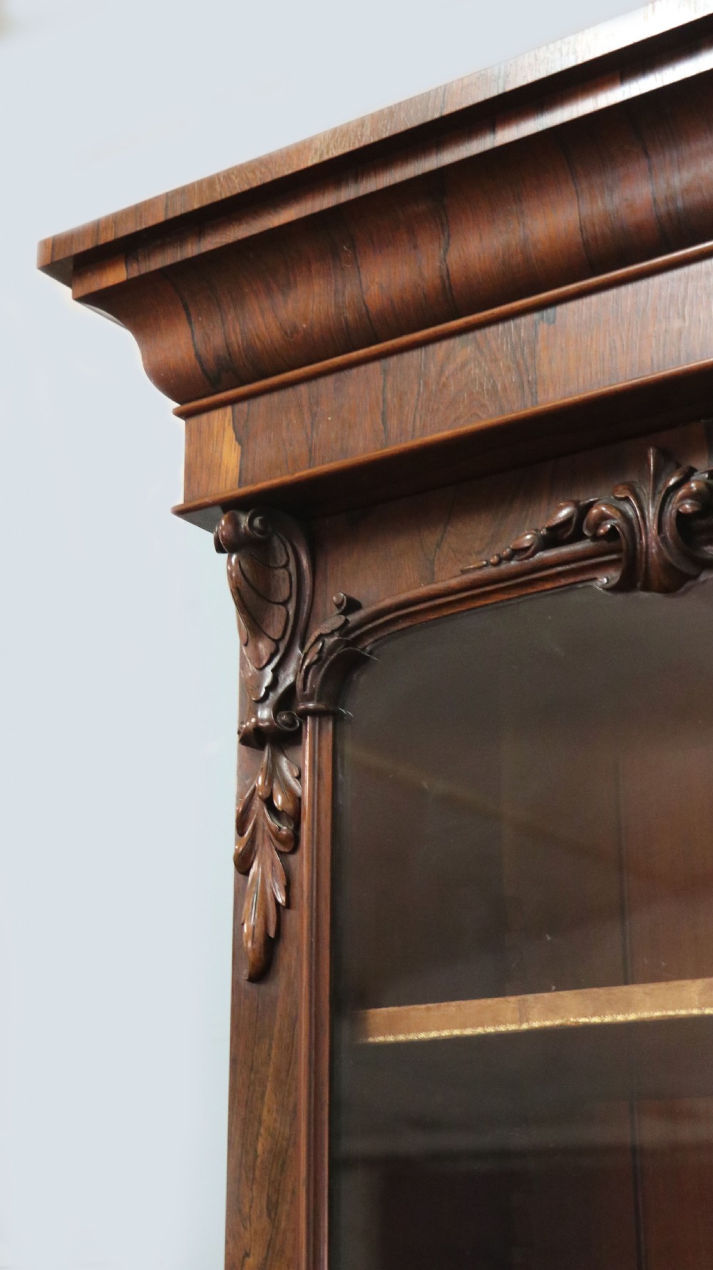 An early Victorian glazed secretaire bookcase cabinet in dark figured wood with carved arch details, a central desk drawer, and lower cupboard doors. View IX