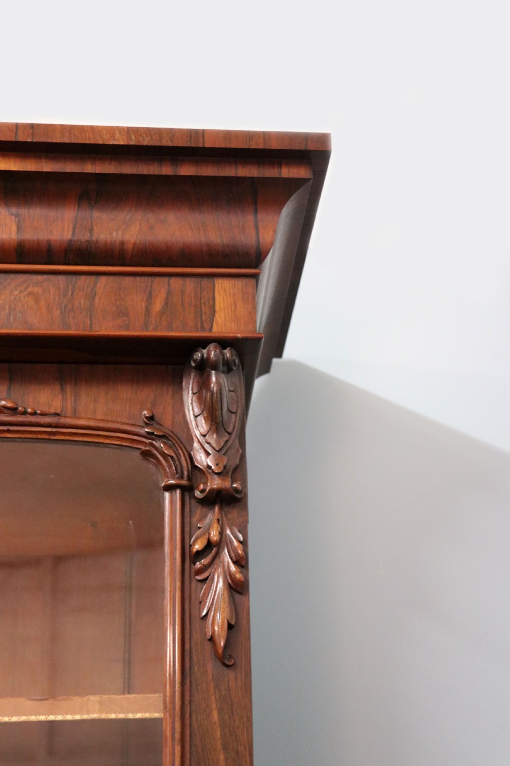An early Victorian glazed secretaire bookcase cabinet in dark figured wood with carved arch details, a central desk drawer, and lower cupboard doors. View XI