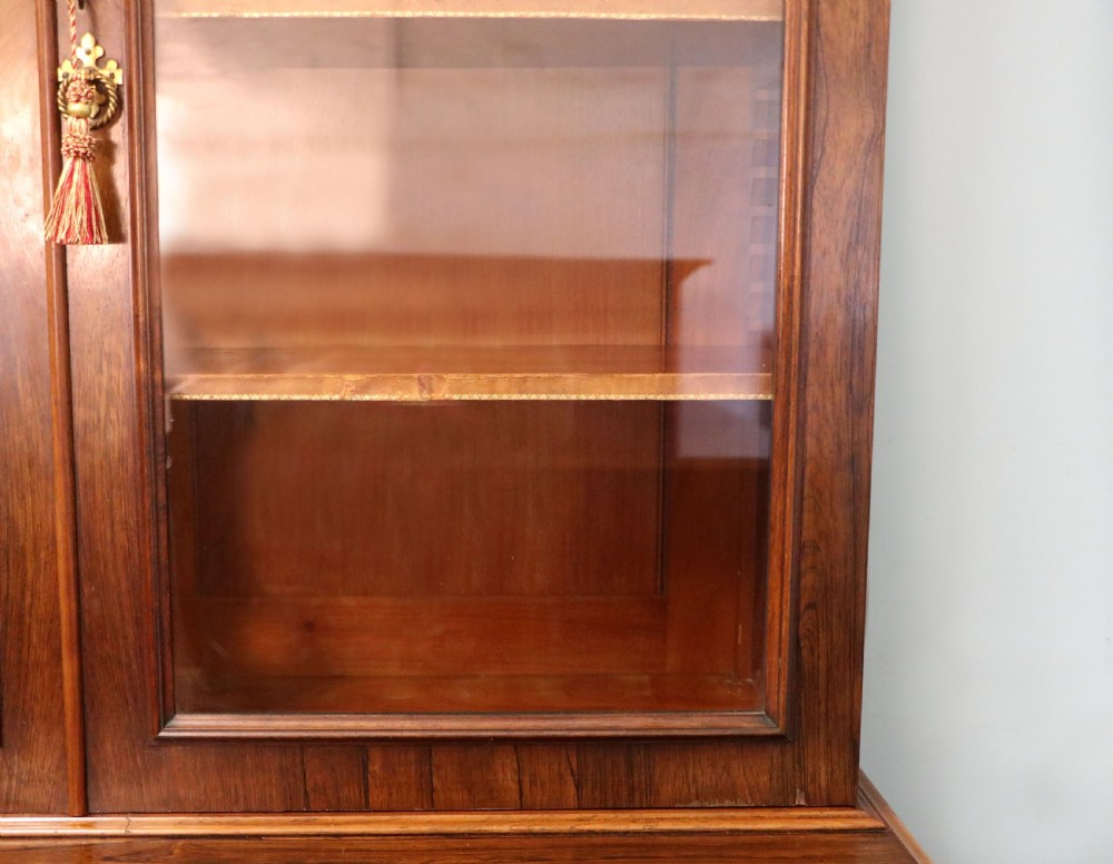 An early Victorian glazed secretaire bookcase cabinet in dark figured wood with carved arch details, a central desk drawer, and lower cupboard doors. View XII