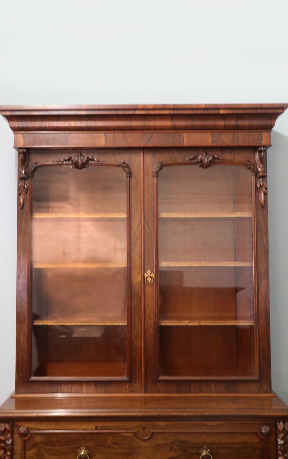 An early Victorian glazed secretaire bookcase cabinet in dark figured wood with carved arch details, a central desk drawer, and lower cupboard doors. View XIII