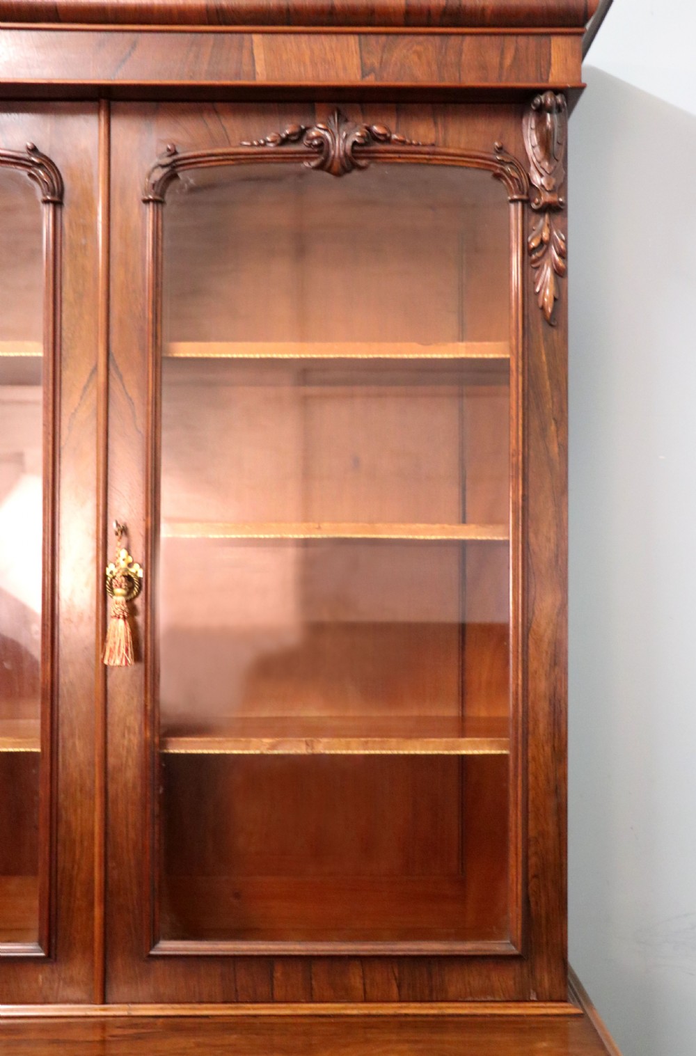 An early Victorian glazed secretaire bookcase cabinet in dark figured wood with carved arch details, a central desk drawer, and lower cupboard doors. View XIV