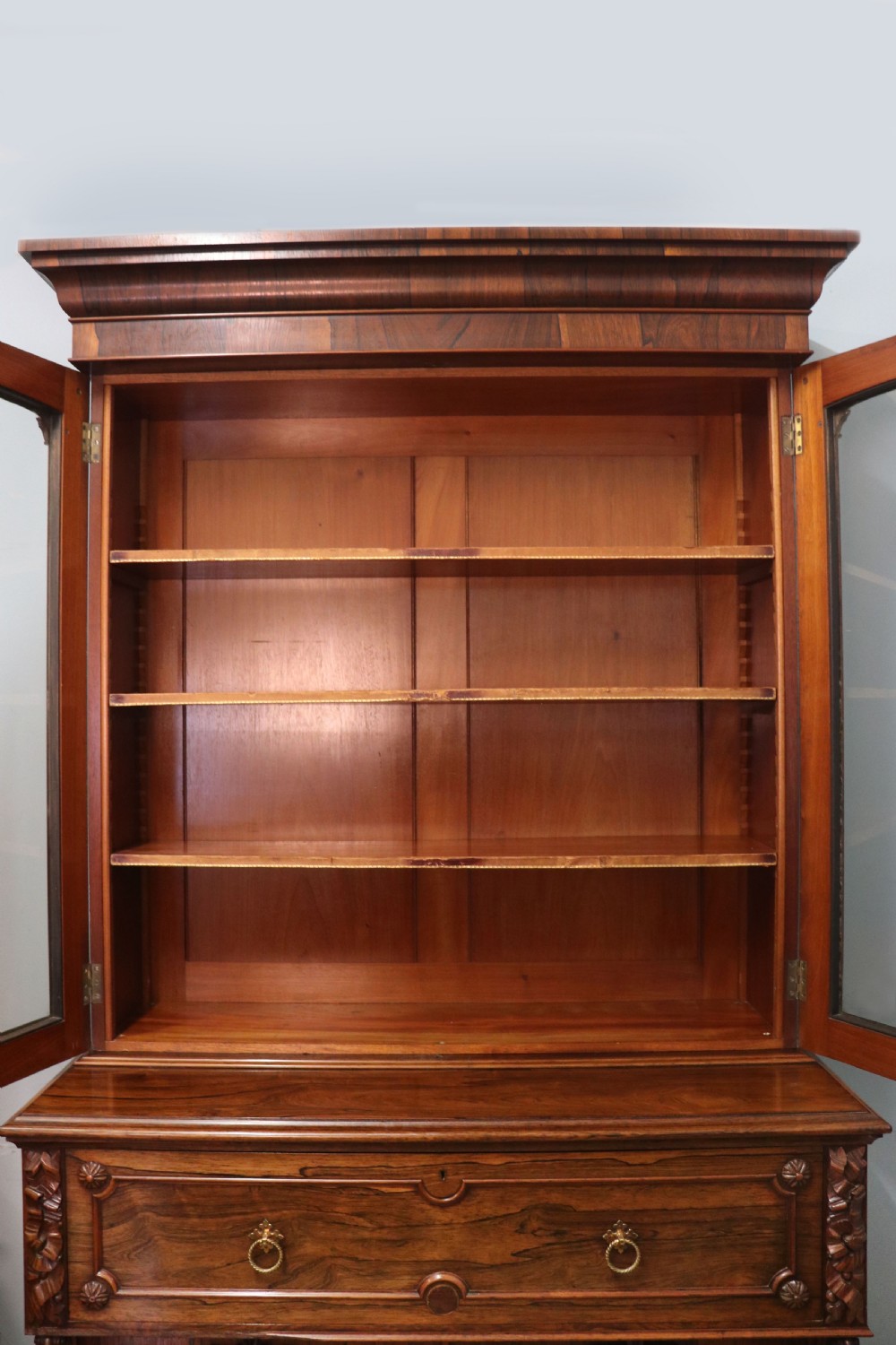 An early Victorian glazed secretaire bookcase cabinet in dark figured wood with carved arch details, a central desk drawer, and lower cupboard doors. View XV
