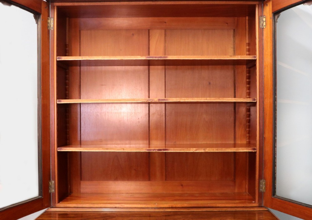 An early Victorian glazed secretaire bookcase cabinet in dark figured wood with carved arch details, a central desk drawer, and lower cupboard doors. View XVI