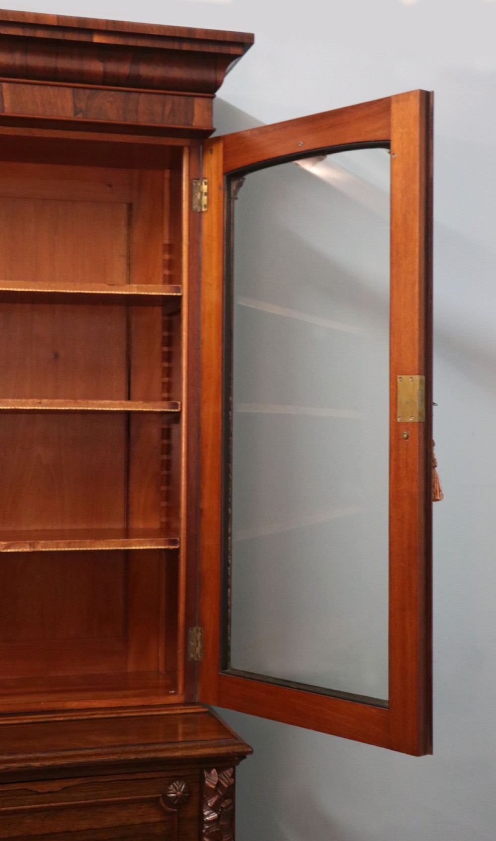 An early Victorian glazed secretaire bookcase cabinet in dark figured wood with carved arch details, a central desk drawer, and lower cupboard doors. View XVII