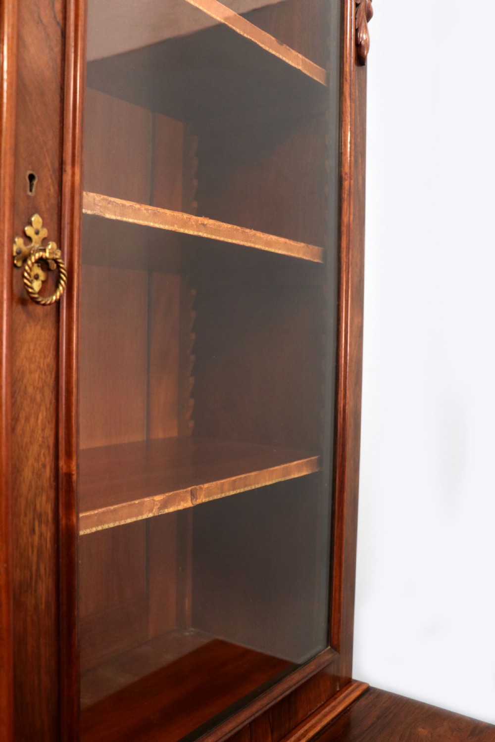 An early Victorian glazed secretaire bookcase cabinet in dark figured wood with carved arch details, a central desk drawer, and lower cupboard doors. View XVIII