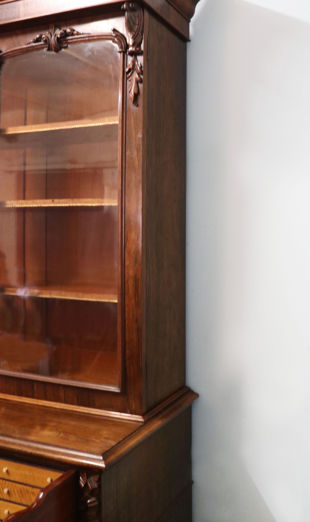 An early Victorian glazed secretaire bookcase cabinet in dark figured wood with carved arch details, a central desk drawer, and lower cupboard doors. View XXI