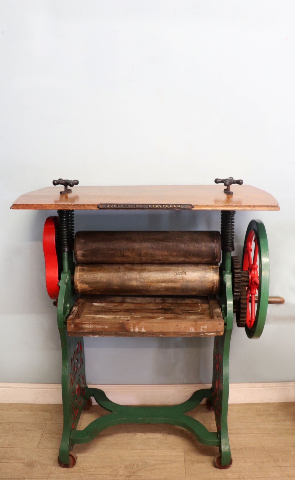 An antique Victorian cast iron mangle with a green and red painted frame, wooden wringer rollers, and a wood tabletop.