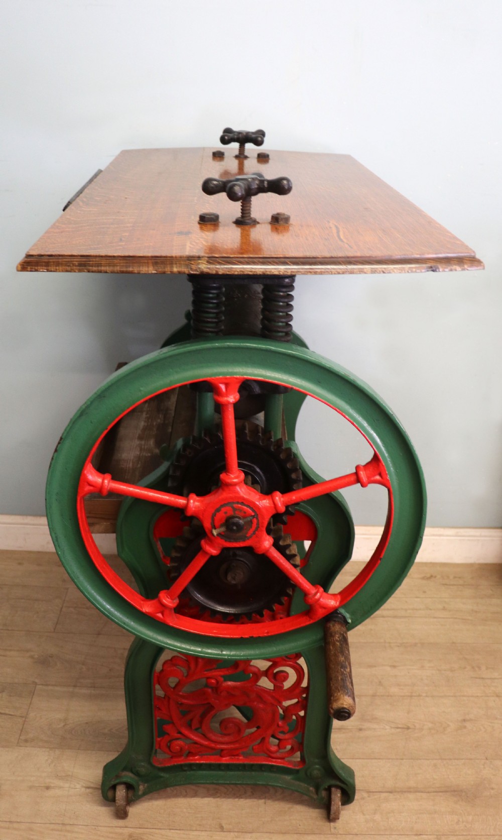 An antique Victorian cast iron mangle with a green and red painted frame, wooden wringer rollers, and a wood tabletop. View II