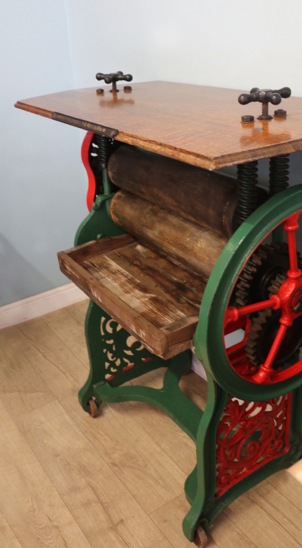 An antique Victorian cast iron mangle with a green and red painted frame, wooden wringer rollers, and a wood tabletop. View III
