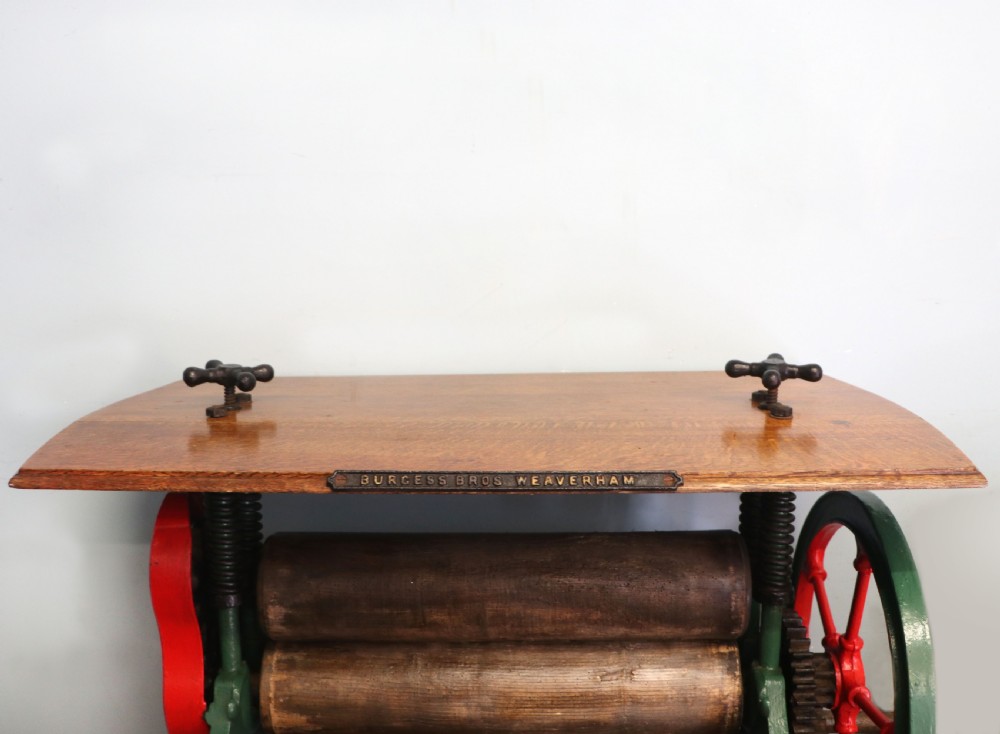 An antique Victorian cast iron mangle with a green and red painted frame, wooden wringer rollers, and a wood tabletop. View IV