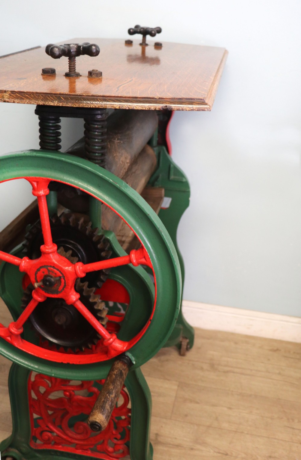 An antique Victorian cast iron mangle with a green and red painted frame, wooden wringer rollers, and a wood tabletop. View VIII
