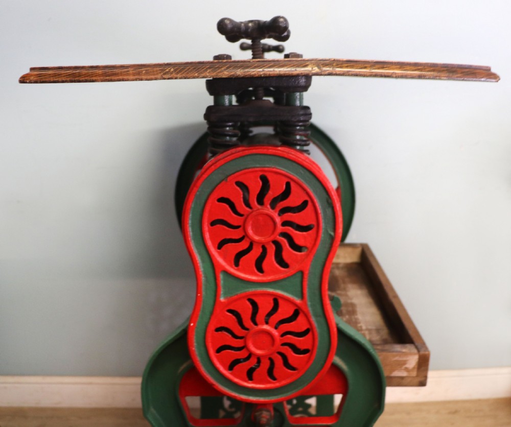 An antique Victorian cast iron mangle with a green and red painted frame, wooden wringer rollers, and a wood tabletop. View IX