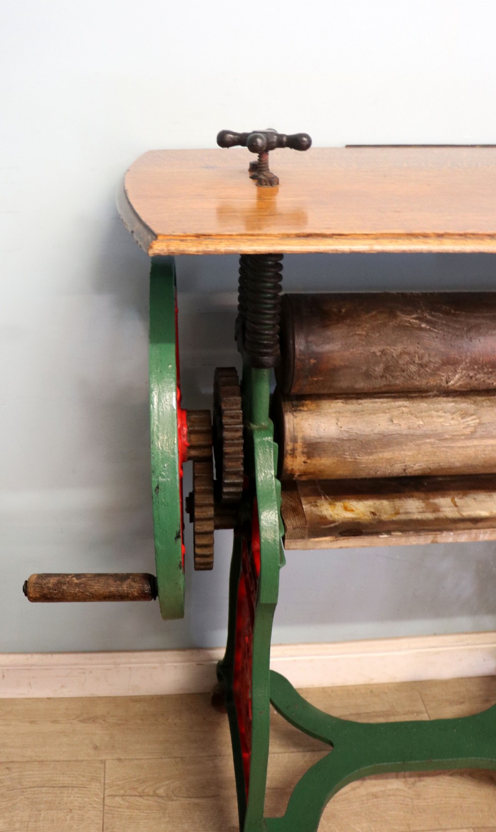 An antique Victorian cast iron mangle with a green and red painted frame, wooden wringer rollers, and a wood tabletop. View XIV