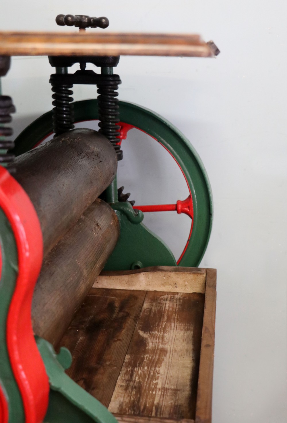 An antique Victorian cast iron mangle with a green and red painted frame, wooden wringer rollers, and a wood tabletop. View XV
