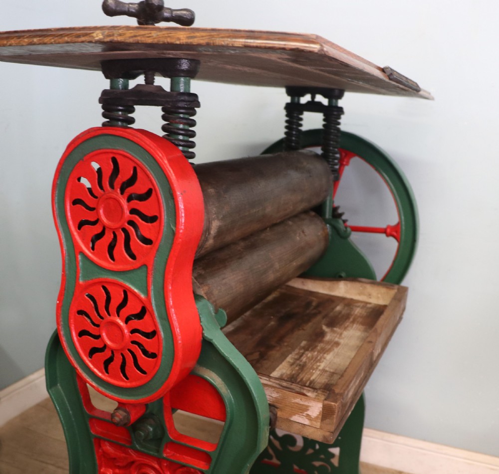 An antique Victorian cast iron mangle with a green and red painted frame, wooden wringer rollers, and a wood tabletop. View XVIII