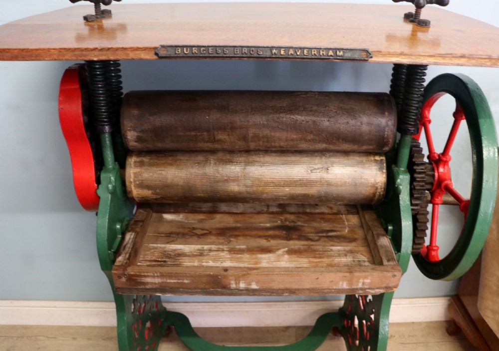 An antique Victorian cast iron mangle with a green and red painted frame, wooden wringer rollers, and a wood tabletop. View XIX
