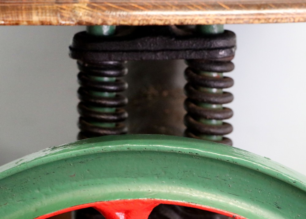An antique Victorian cast iron mangle with a green and red painted frame, wooden wringer rollers, and a wood tabletop. View XX