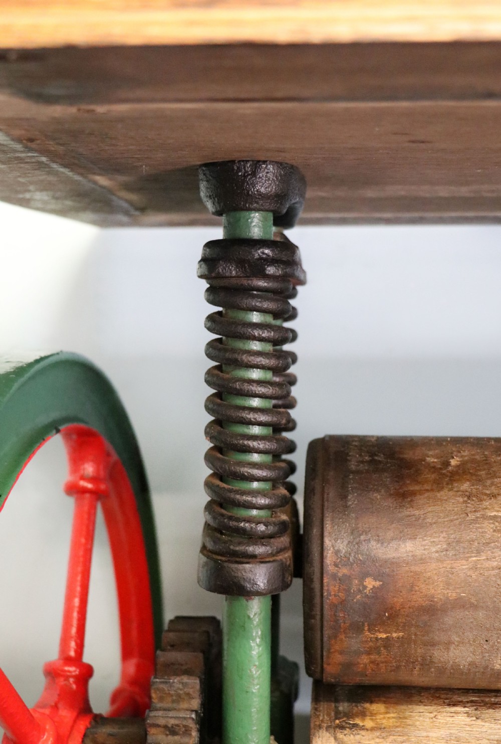 An antique Victorian cast iron mangle with a green and red painted frame, wooden wringer rollers, and a wood tabletop. View XXI
