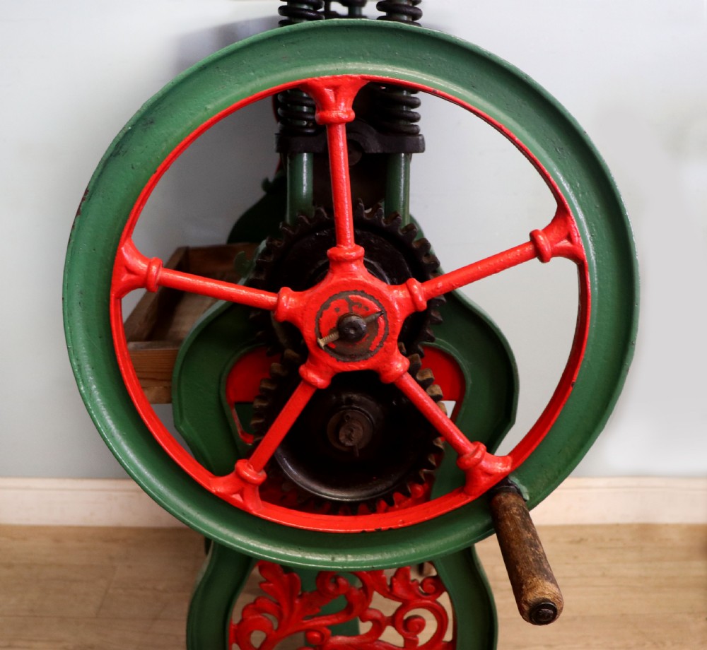 An antique Victorian cast iron mangle with a green and red painted frame, wooden wringer rollers, and a wood tabletop. View XXIV