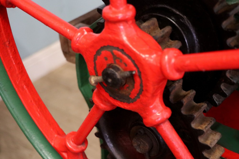 An antique Victorian cast iron mangle with a green and red painted frame, wooden wringer rollers, and a wood tabletop. View XXVI