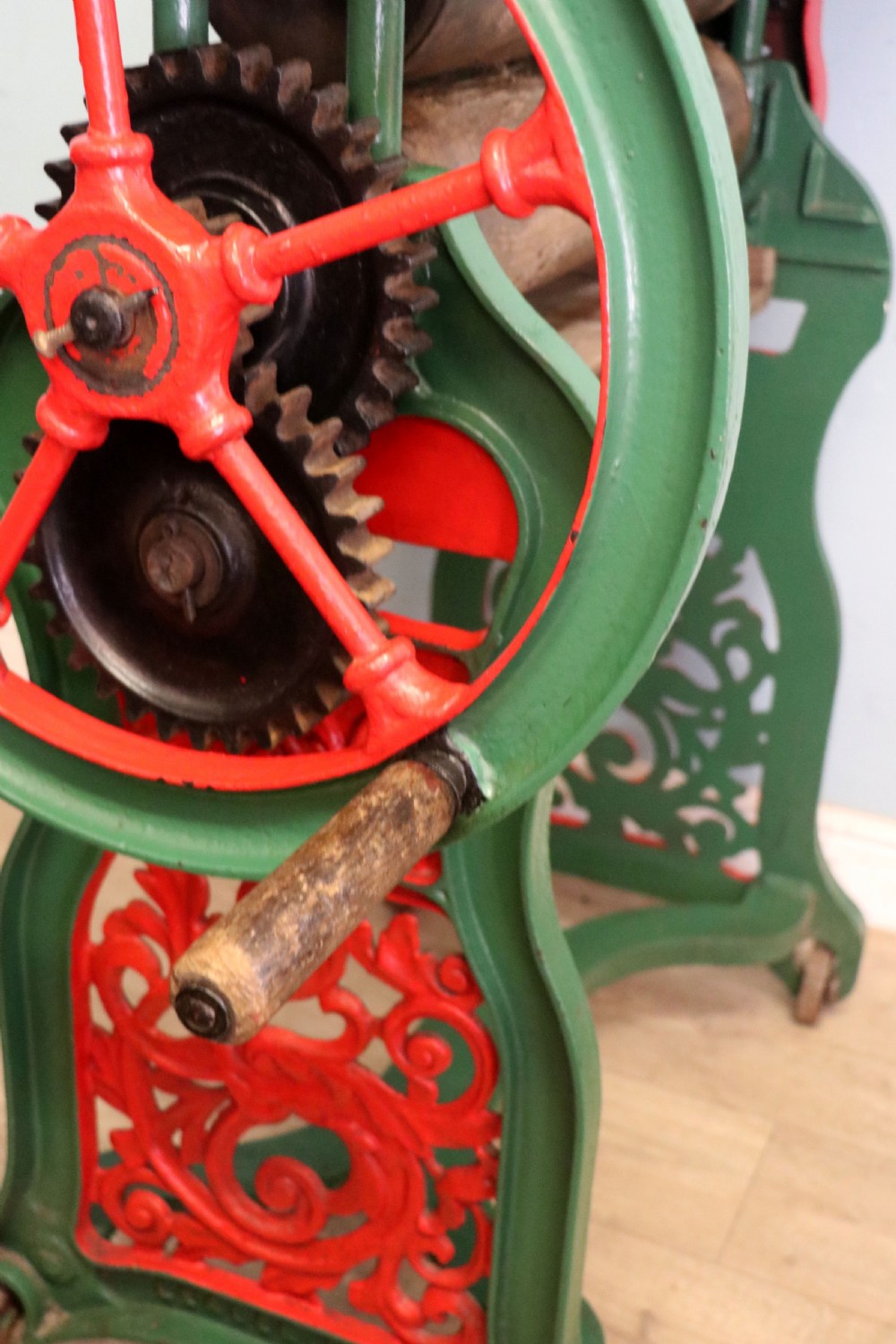 An antique Victorian cast iron mangle with a green and red painted frame, wooden wringer rollers, and a wood tabletop. View XXVIII