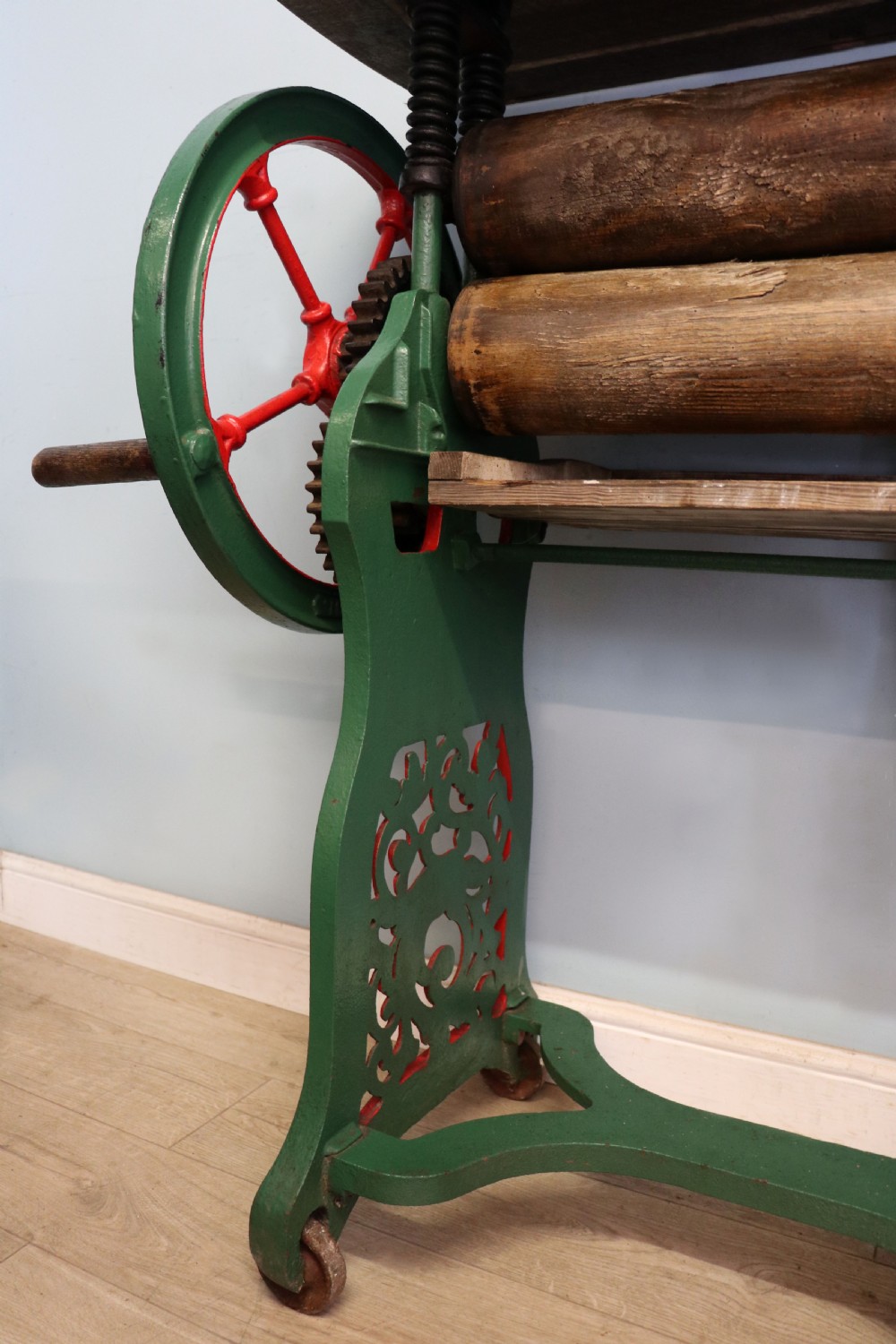 An antique Victorian cast iron mangle with a green and red painted frame, wooden wringer rollers, and a wood tabletop. View XXX