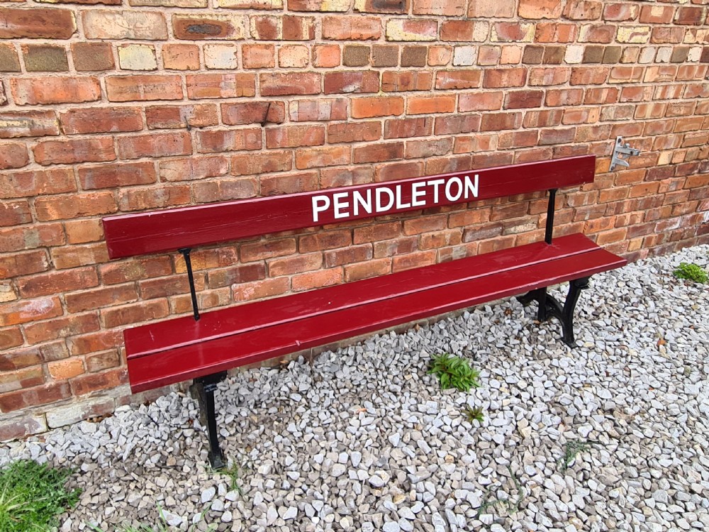 A late nineteenth-century railway station bench with deep red painted wooden slats displaying white stencilled lettering that reads PENDLETON, supported on black cast iron legs. View IV
