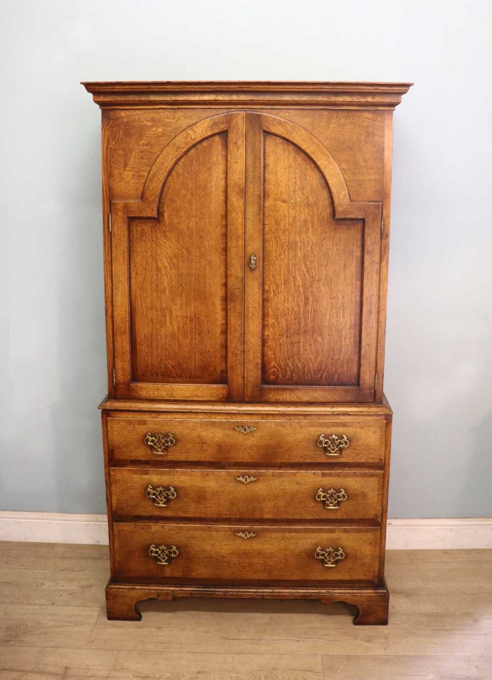 A Georgian style warm brown oak bureau cabinet featuring two upper arched doors opening to a fitted interior of pigeonholes and small drawers above three long drawers with brass handles. View III